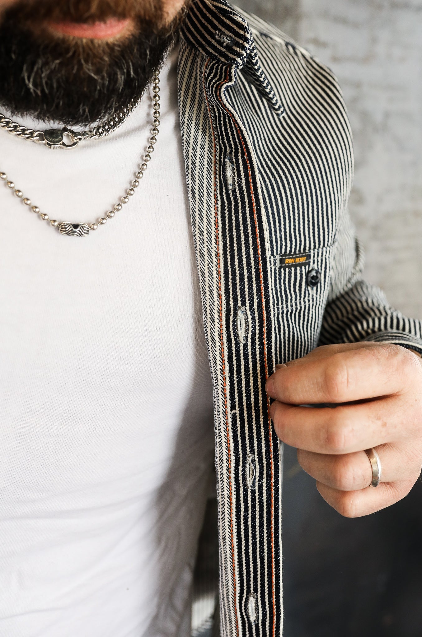 Man wearing a striped Iron Heart jacket over white shirt, showing button details and silver necklace