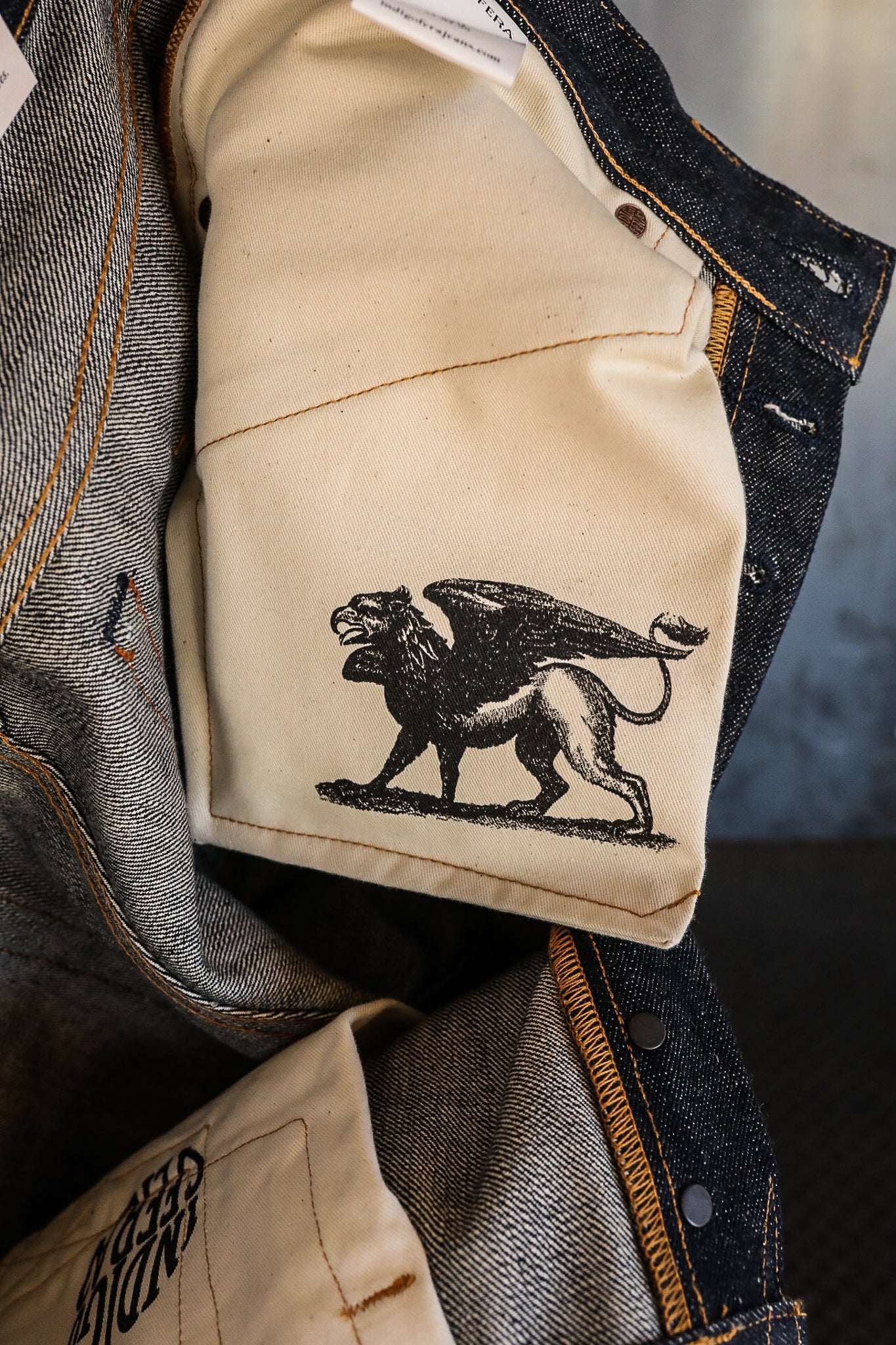Inside pocket of dark denim jacket featuring beige fabric and black griffin print, detailed stitching, and metal snap buttons