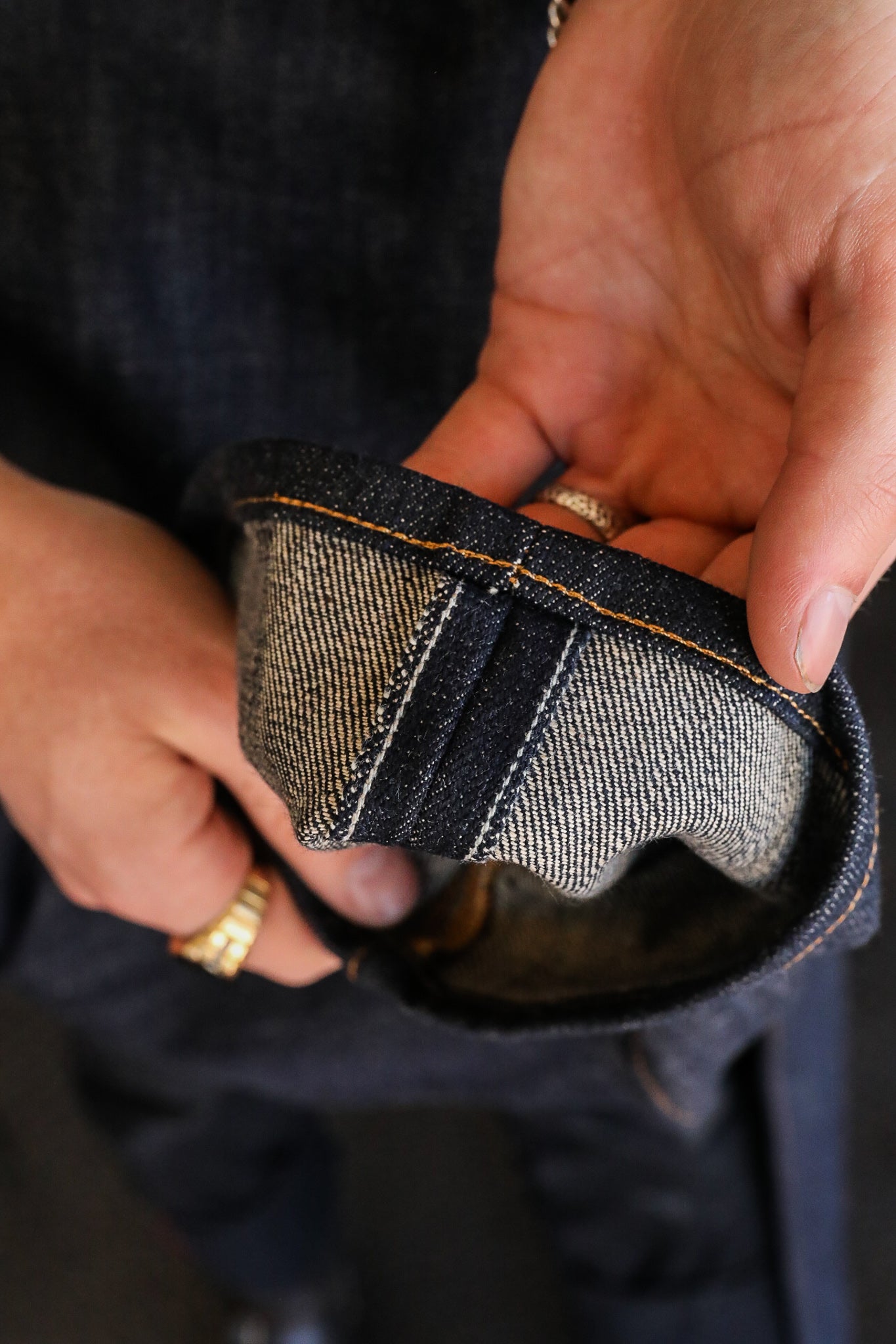 Close-up of hands holding the cuff of raw selvedge denim jeans with detailed stitching