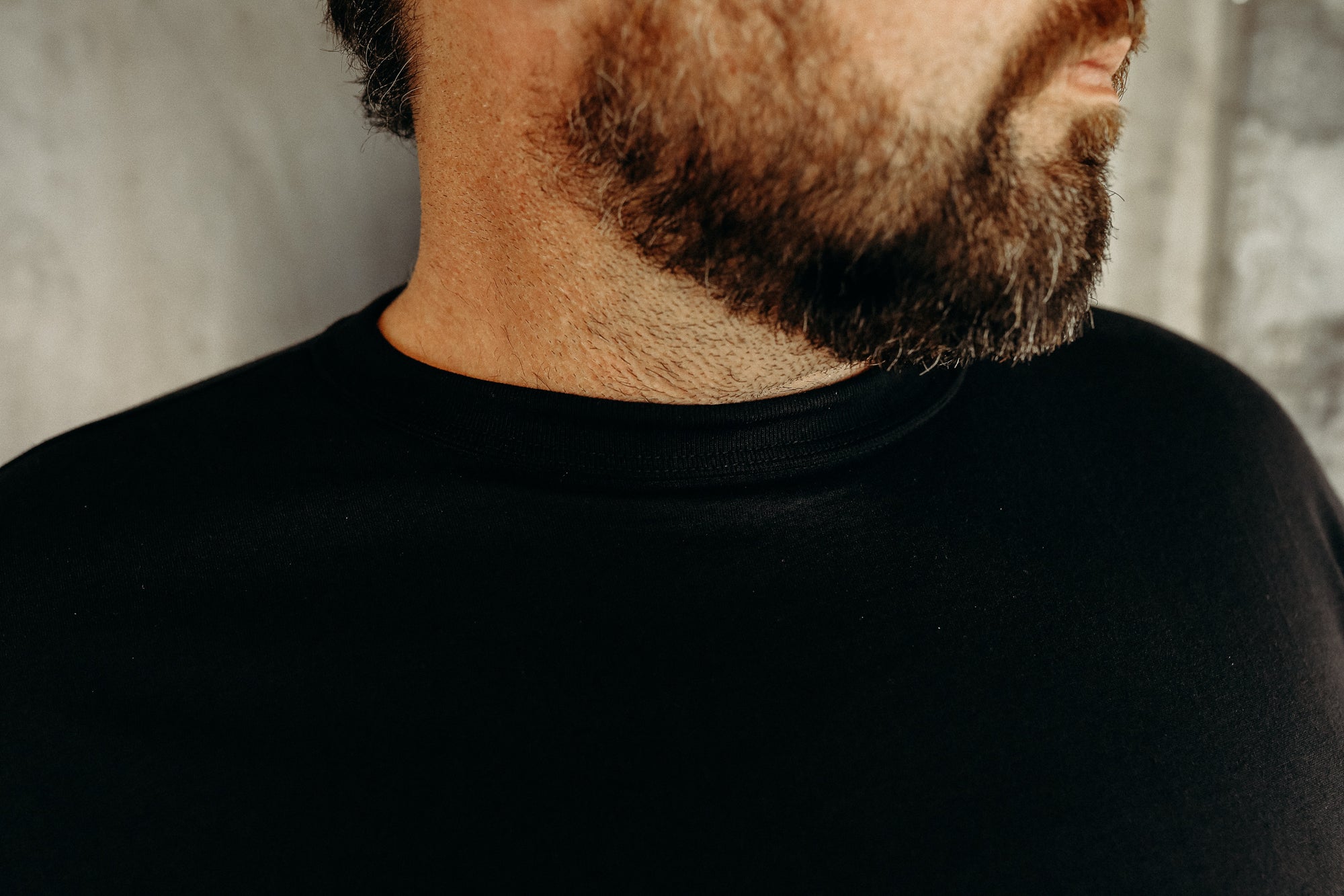 Close-up of a bearded man wearing a black crew neck shirt against a neutral background