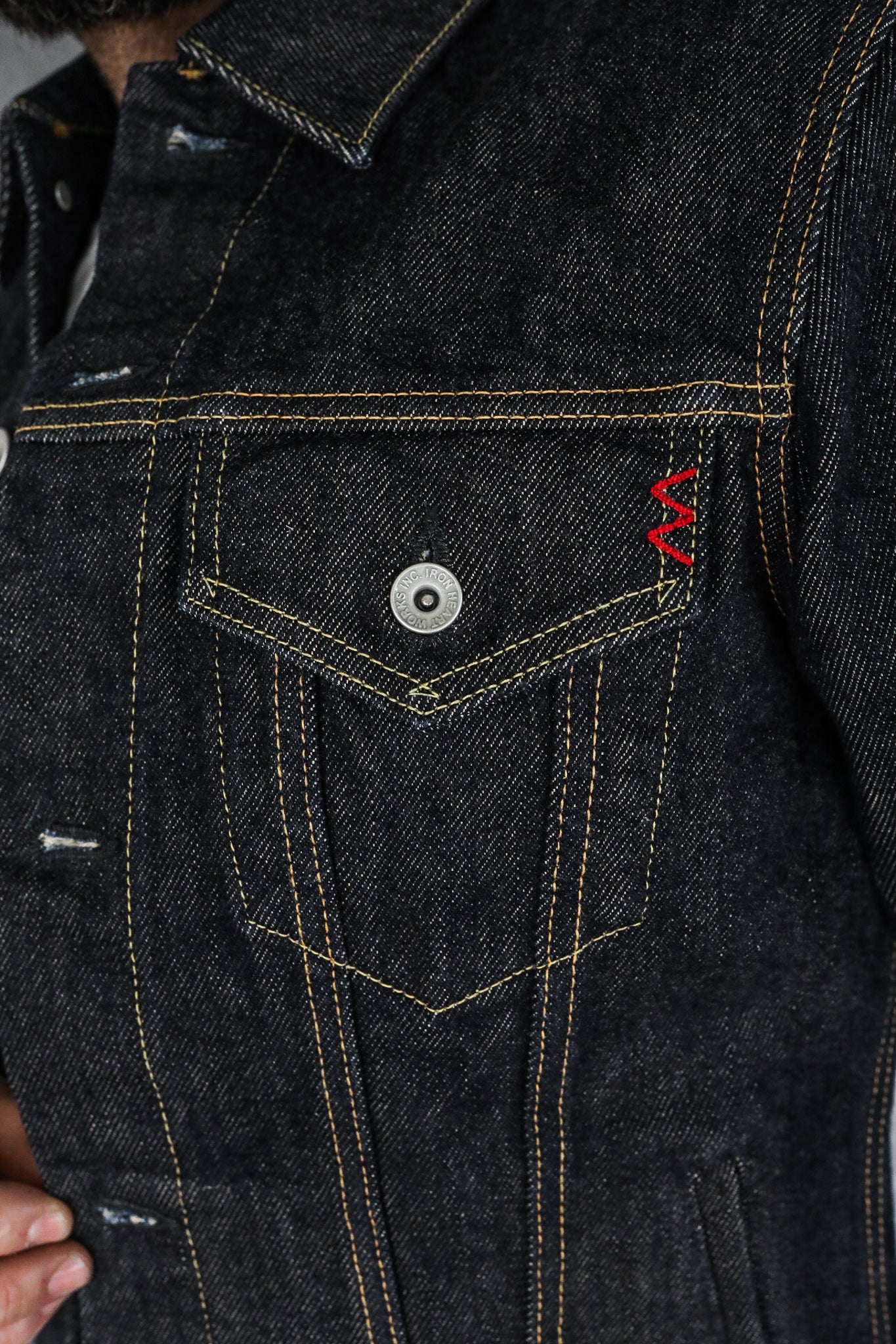 Close-up of dark denim jacket pocket with contrast yellow stitching and red embroidered detail at Iron Shop Provisions