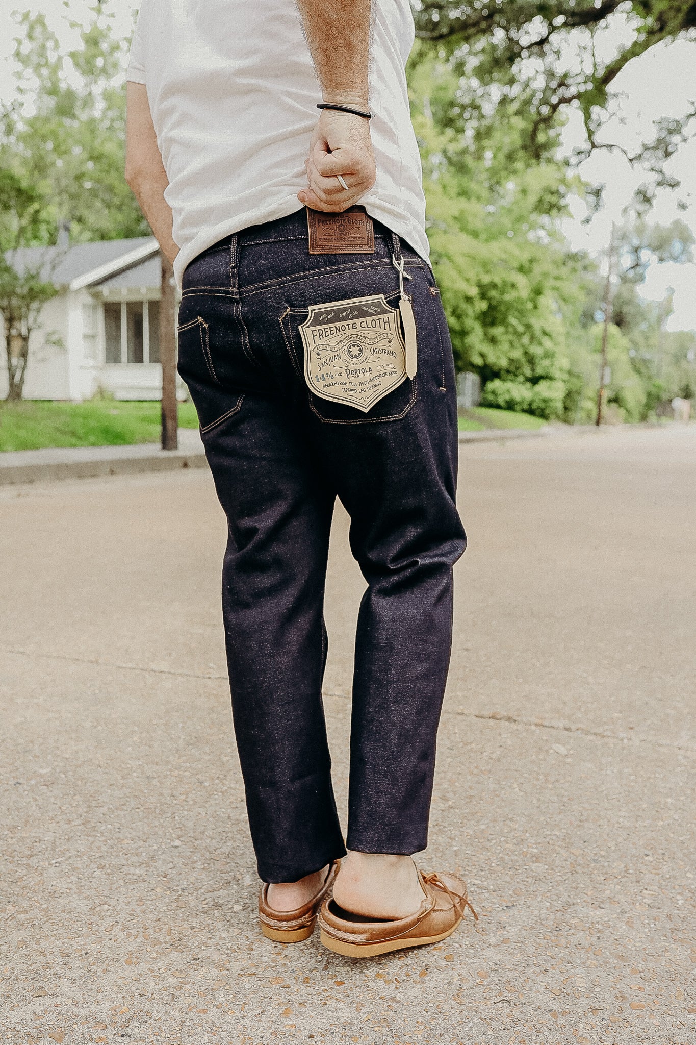 Man wearing dark raw denim jeans with Freenote Cloth label outdoors on street in casual shoes