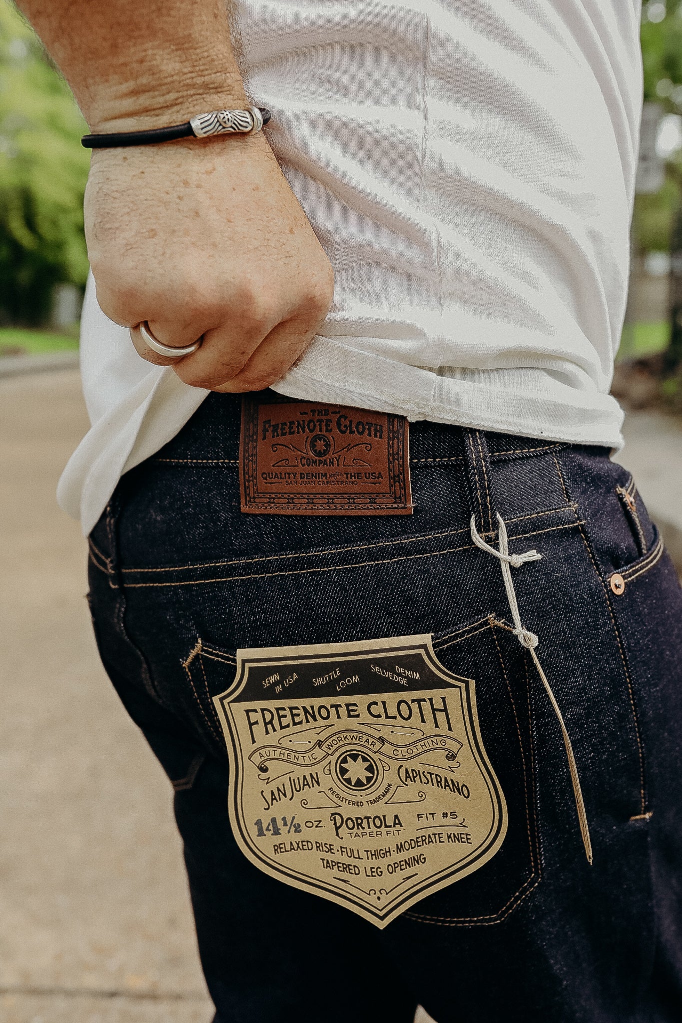 Close-up of person wearing Freenote Cloth dark denim jeans with label and white t-shirt outdoors