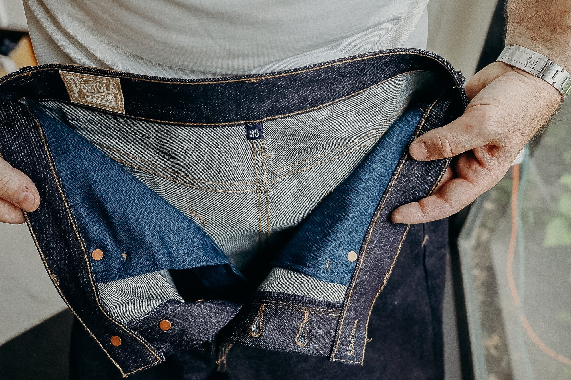 Close-up of hands holding dark denim jeans showing inner blue lining and size 33 tag