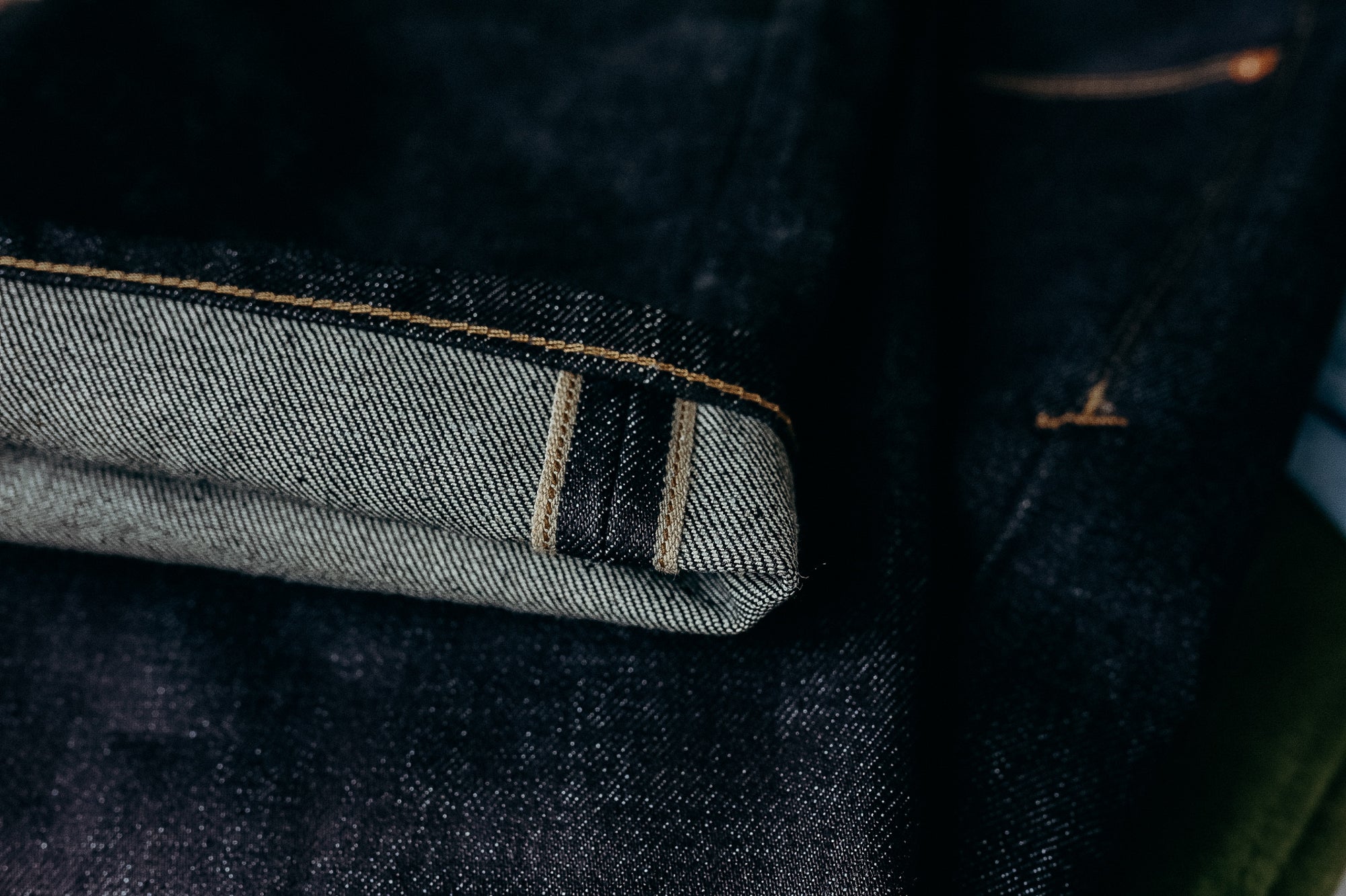 Close-up of dark raw selvedge denim jeans with visible cuff and orange stitching