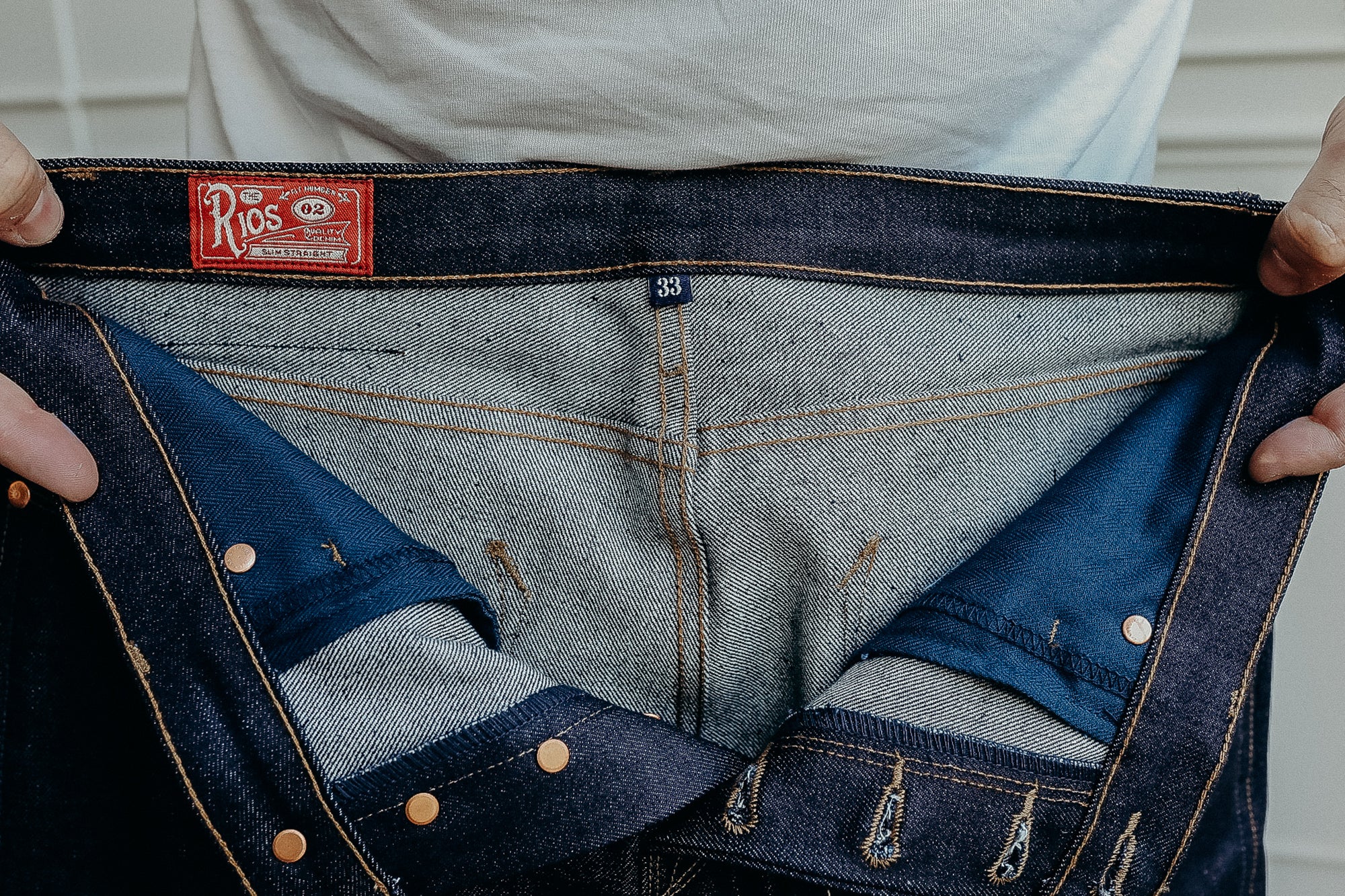 Hands holding open dark blue Rios slim straight denim jeans showing inner stitching and size 33 tag