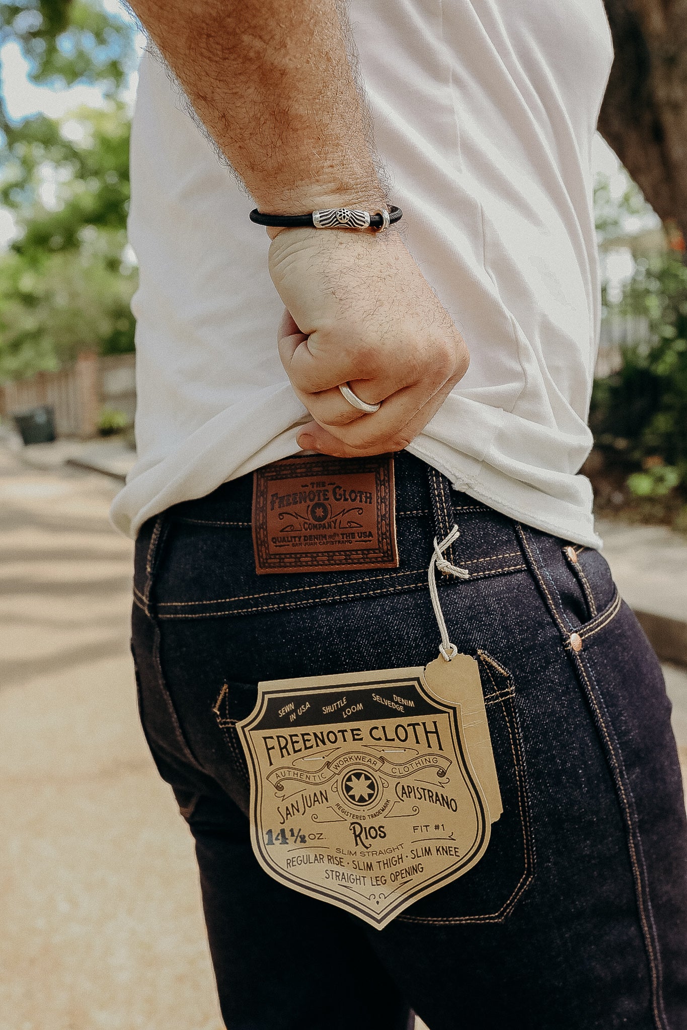 Close-up of person wearing dark Freenote Cloth denim jeans with leather patch and attached tag outdoors