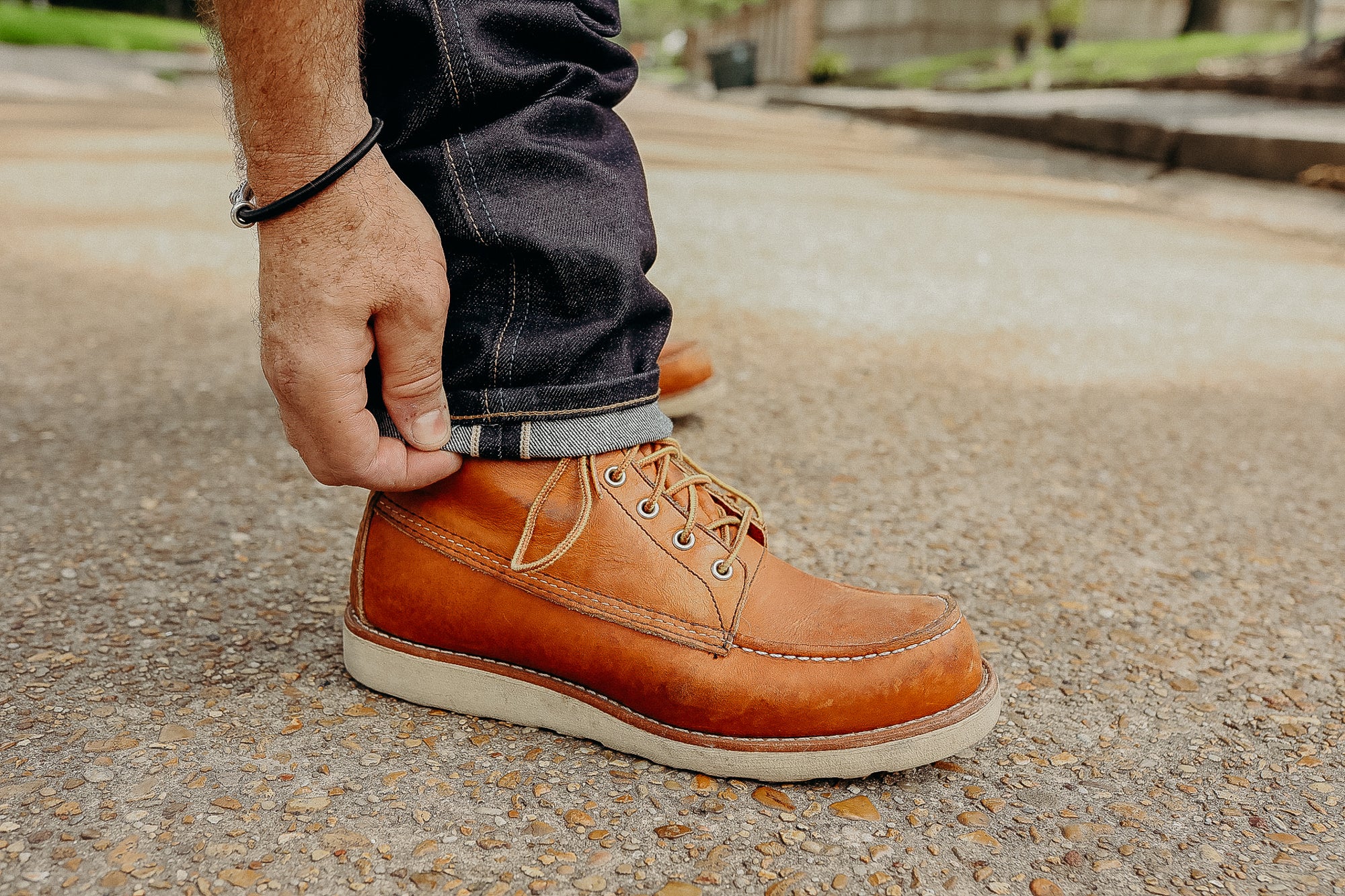 Close-up of hand rolling up dark denim jeans above tan leather boots on textured pavement