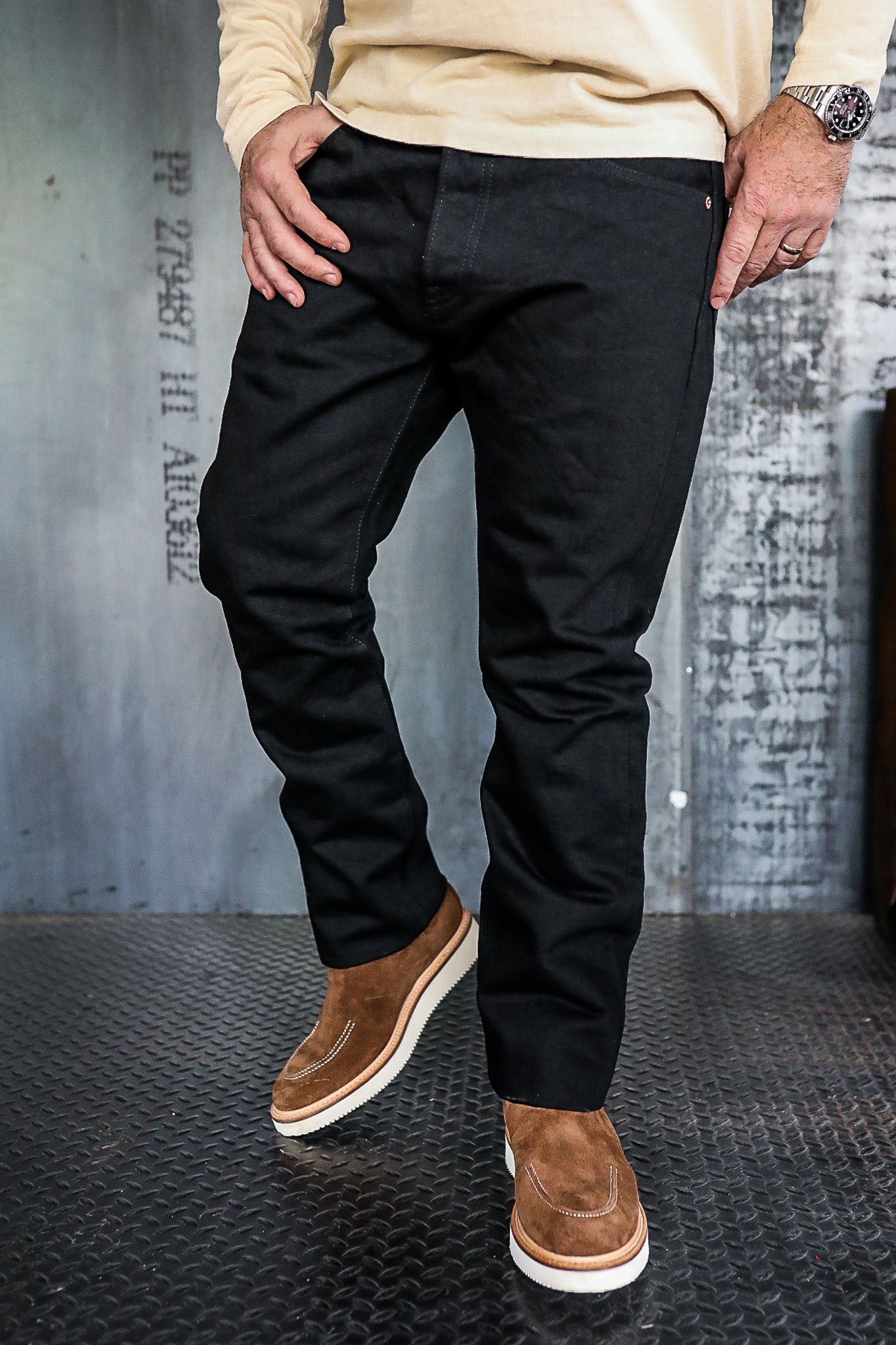 Man wearing black work pants and brown suede boots standing on industrial metal floor