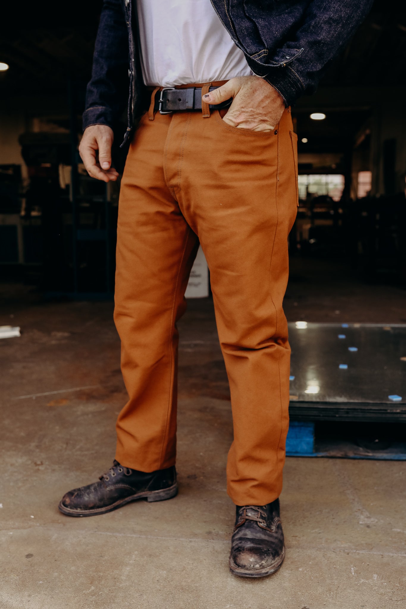 Man wearing brown work pants with black belt and worn black work boots in industrial workshop