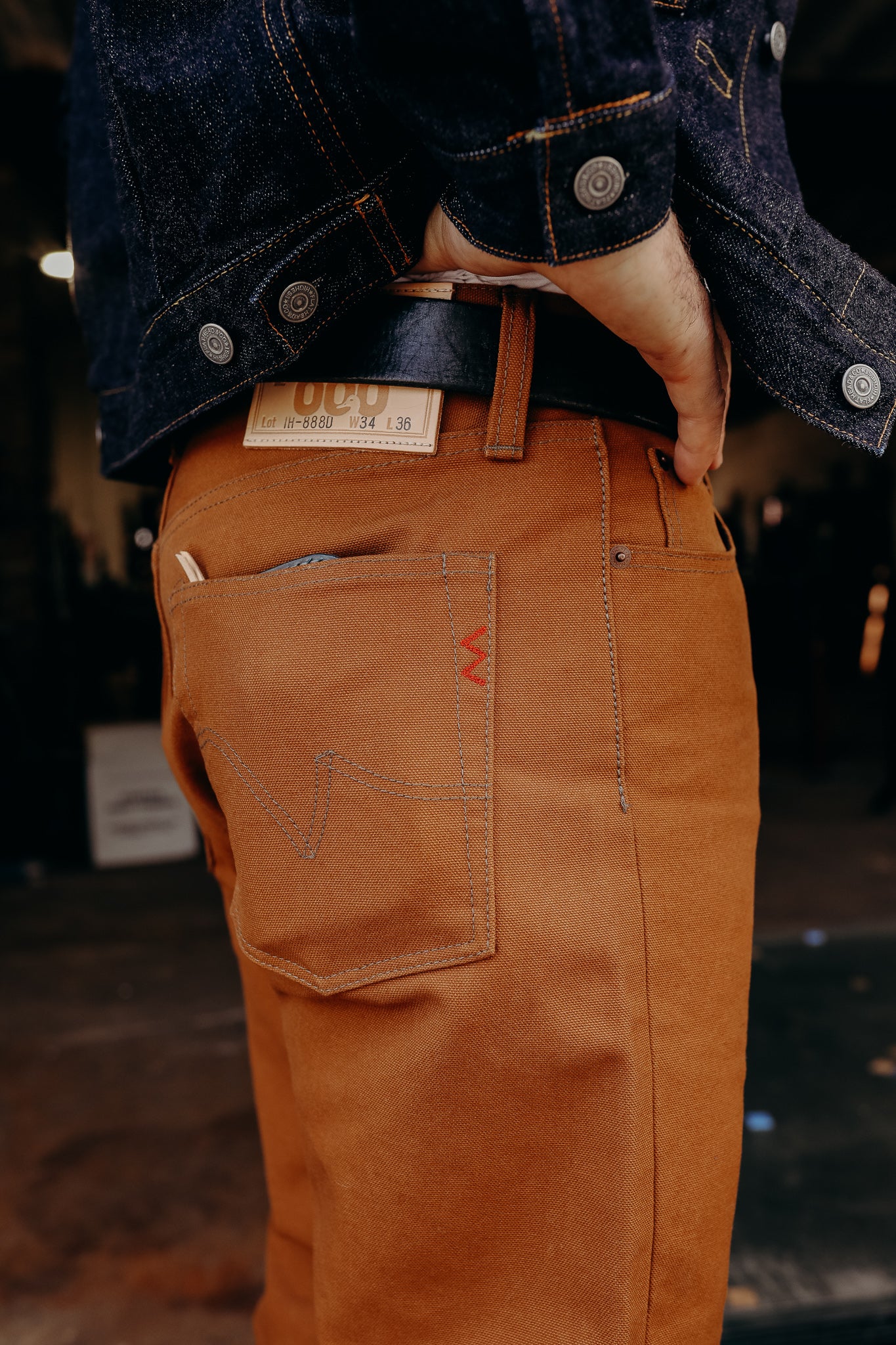 Close-up of a person wearing brown canvas work pants with a leather belt and dark denim jacket