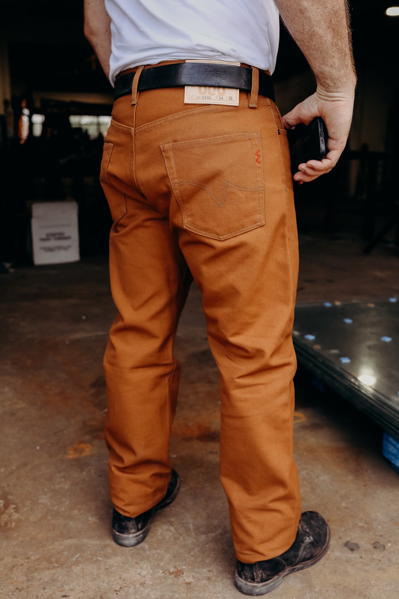 Man wearing durable brown work pants with black belt and boots standing in industrial workspace