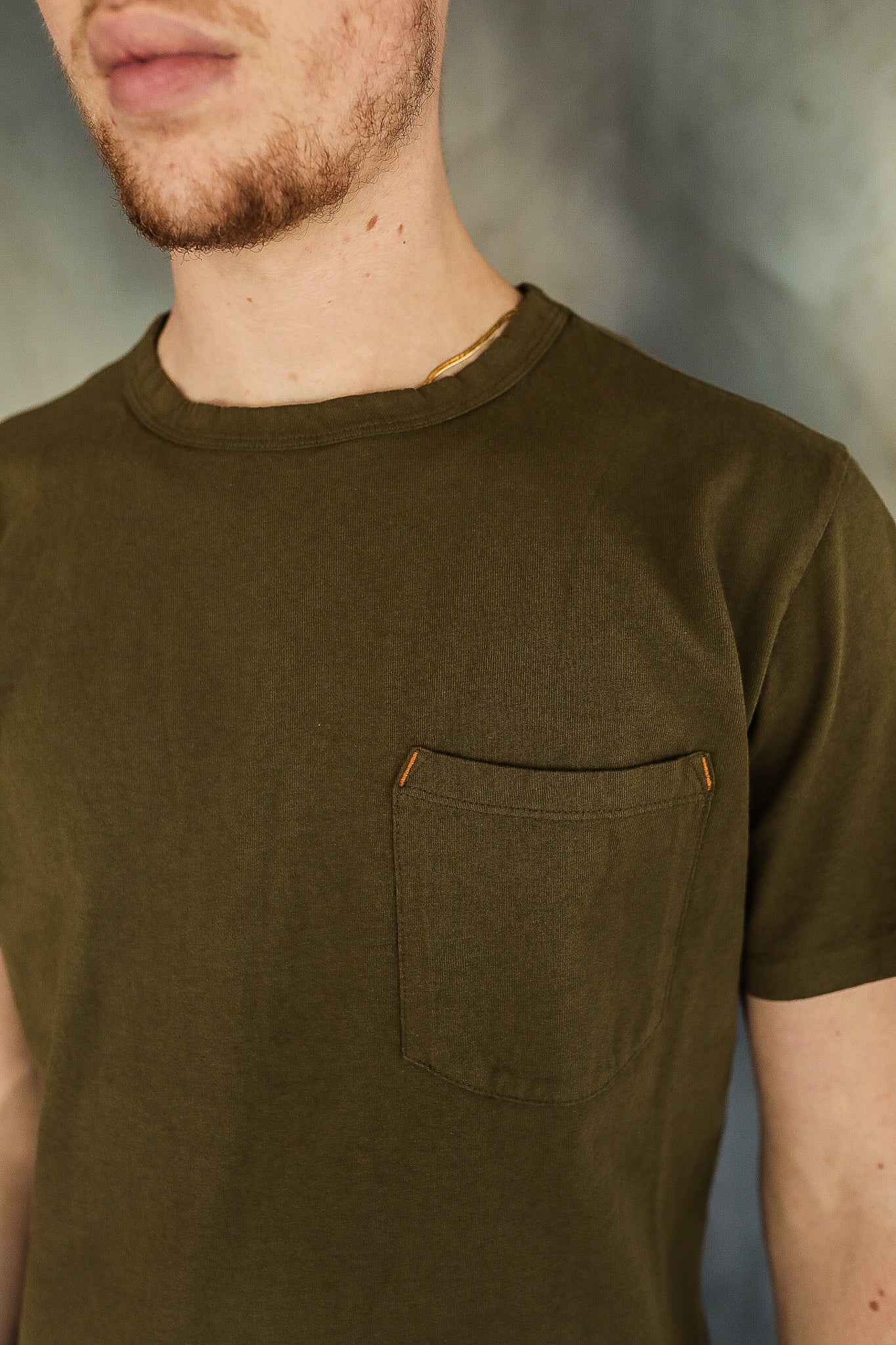 Close-up of man wearing olive green pocket t-shirt with orange stitch accents from Iron Shop Provisions