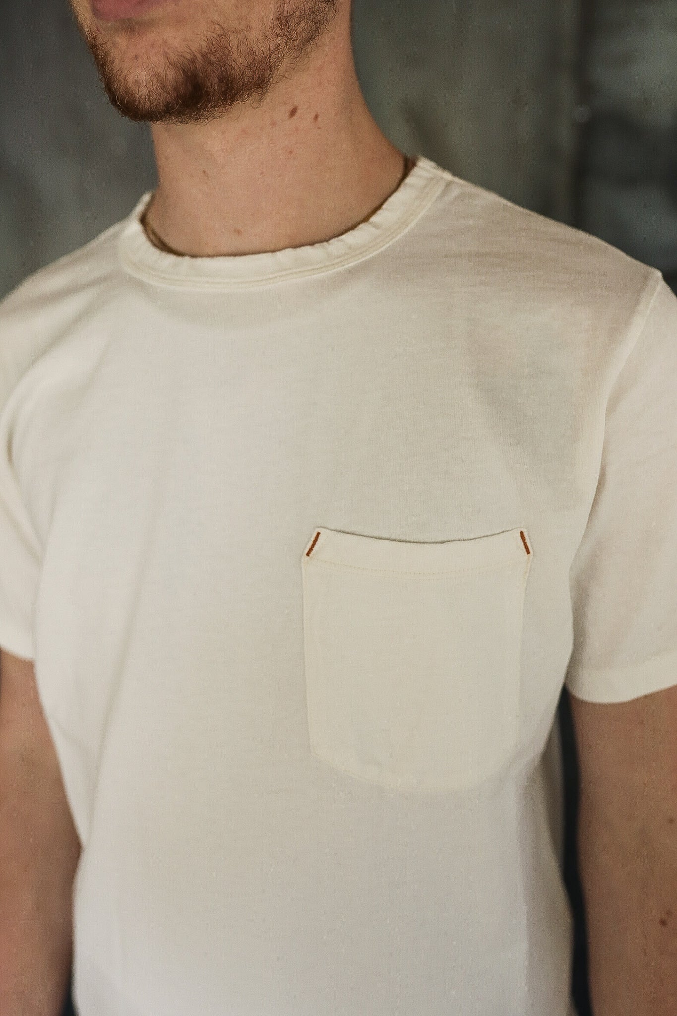 Close-up of man wearing a cream-colored crew neck T-shirt with a chest pocket and subtle brown stitch accents