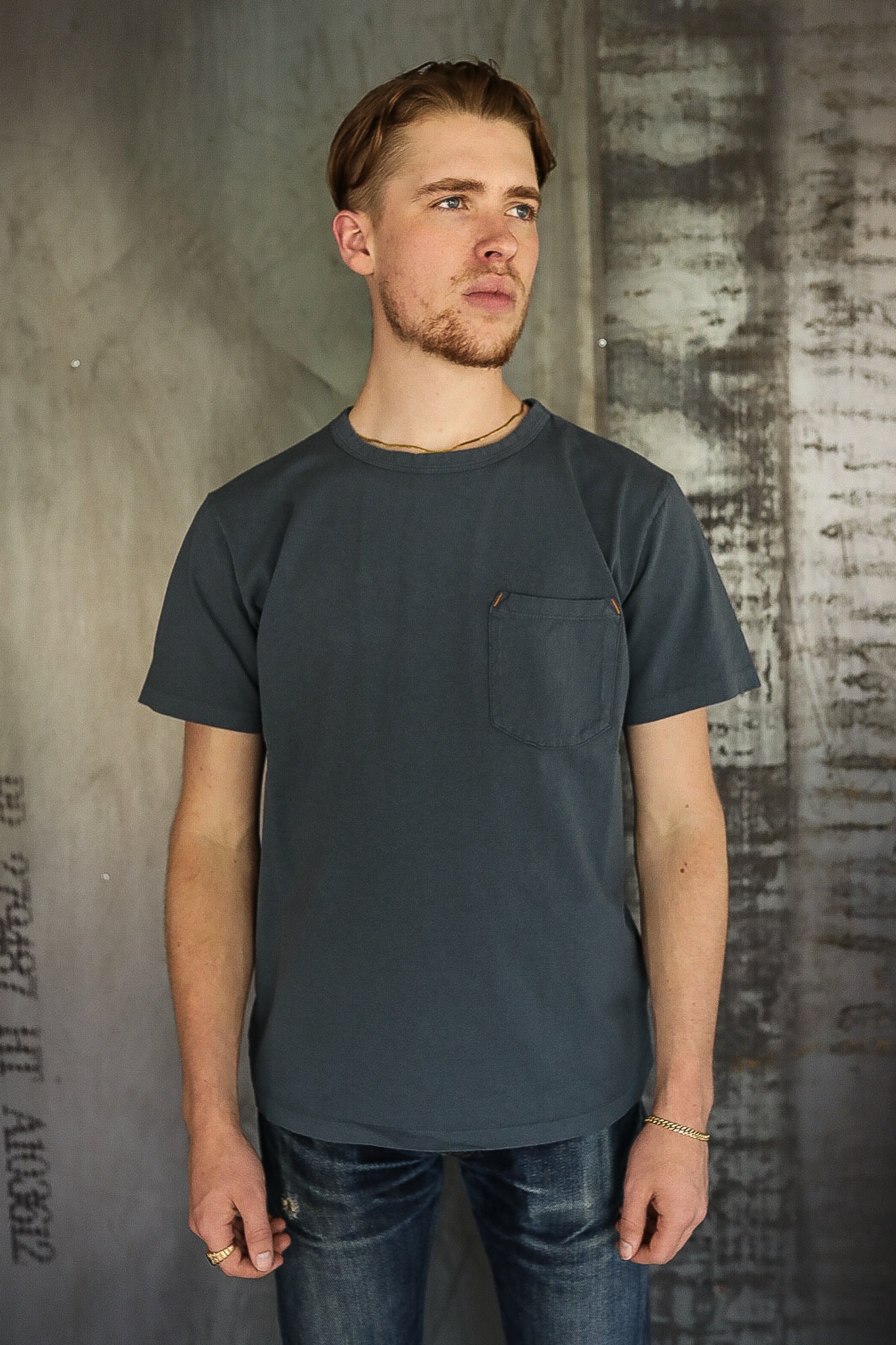 Young man wearing dark gray pocket t-shirt and distressed jeans in industrial setting