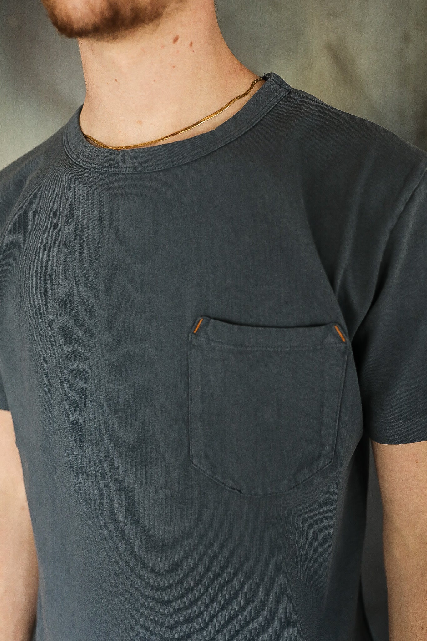 Close-up of man wearing charcoal gray pocket T-shirt with crew neckline and gold chain necklace