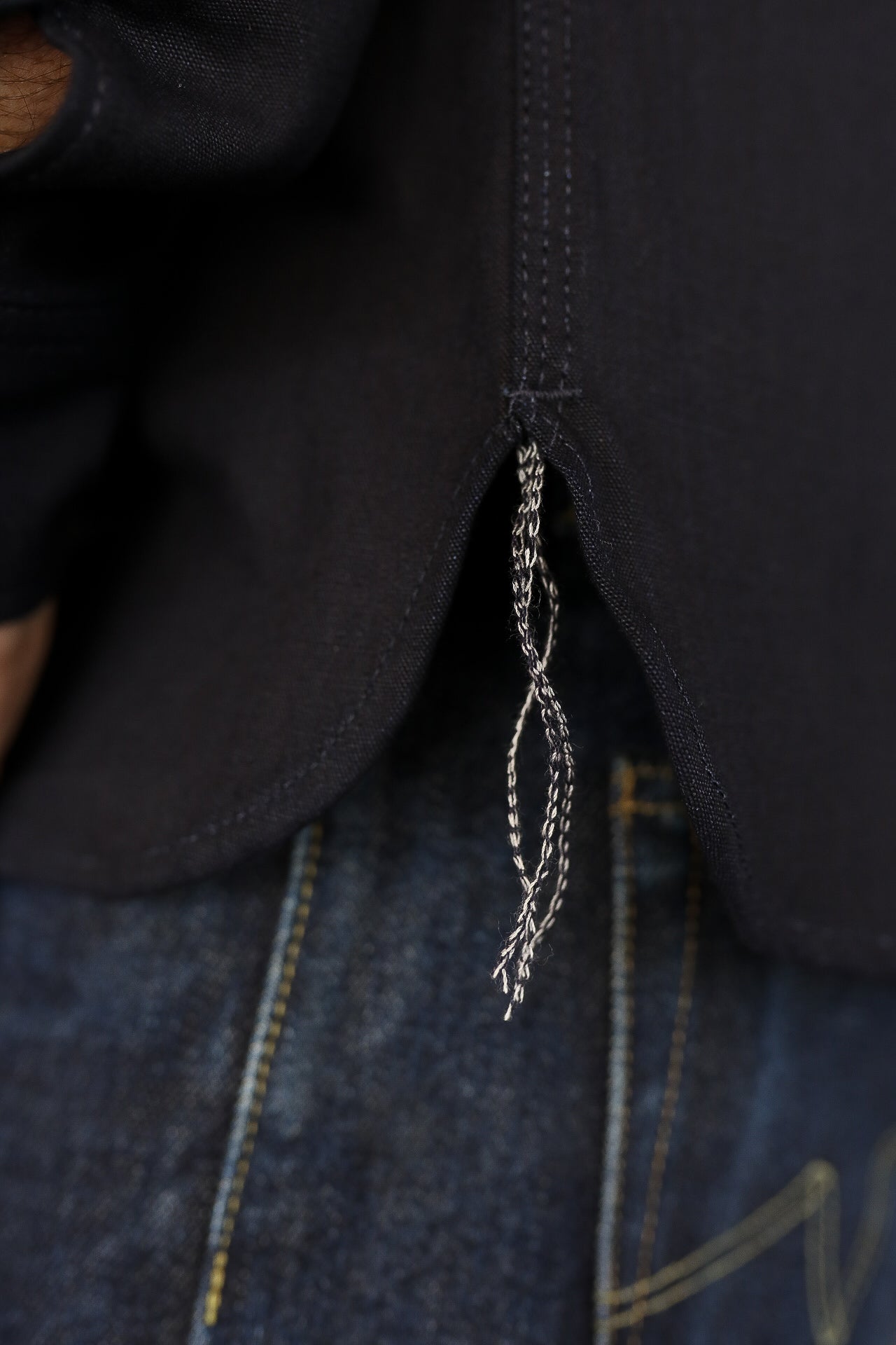 Close-up of black fabric shirt hem with loose white stitching threads over blue denim jeans