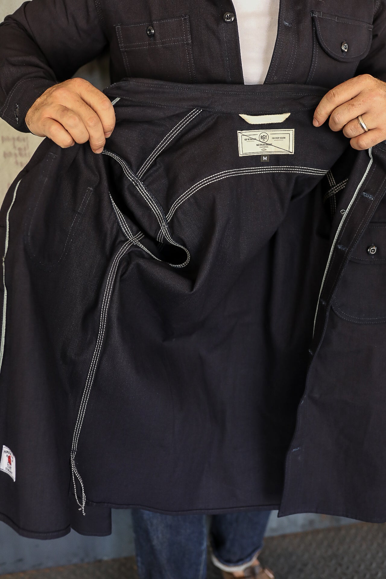 Person holding open a dark denim chore coat showing detailed white stitching and inside label size medium
