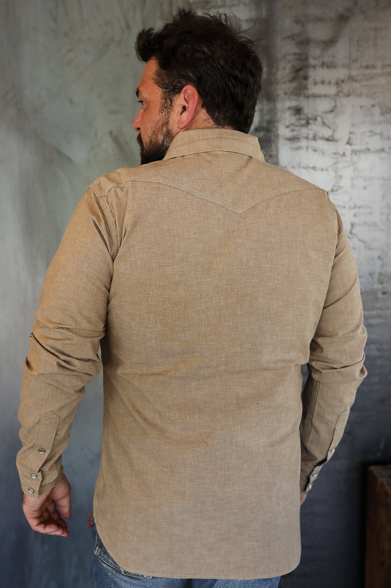 Man wearing tan casual long sleeve shirt standing against textured wall