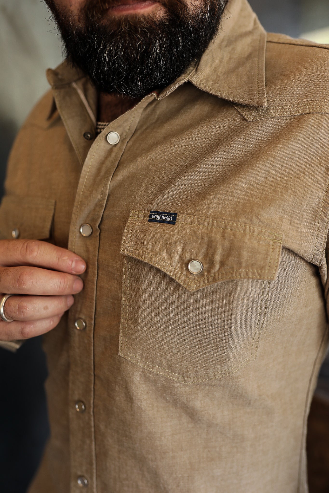 Close-up of a man wearing a beige Iron Heart button-up shirt with snap buttons and chest pockets