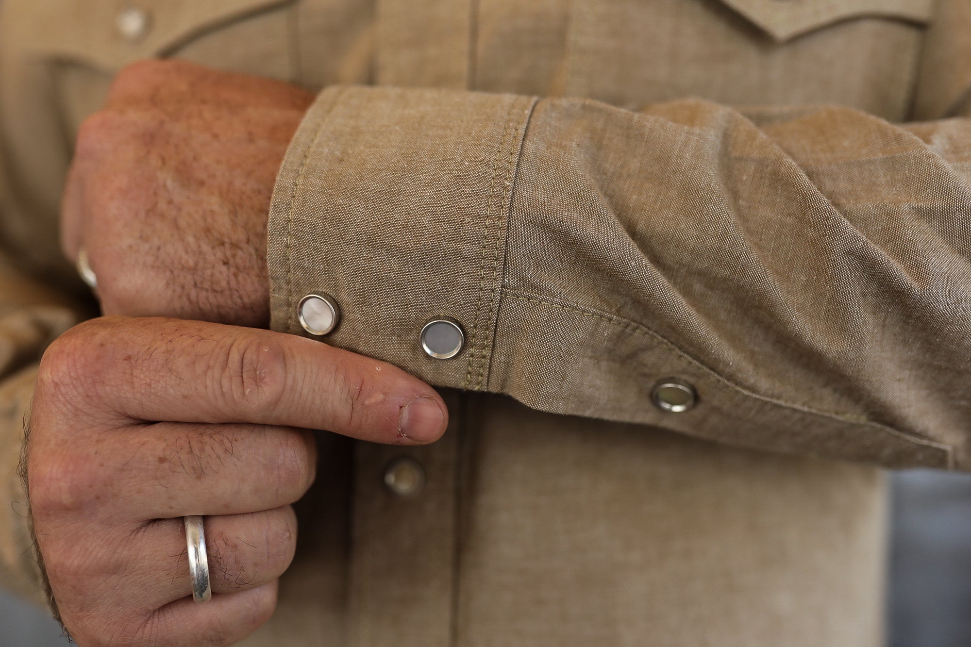 Close-up of a man's hand adjusting the cuff of a tan work shirt with silver snap buttons