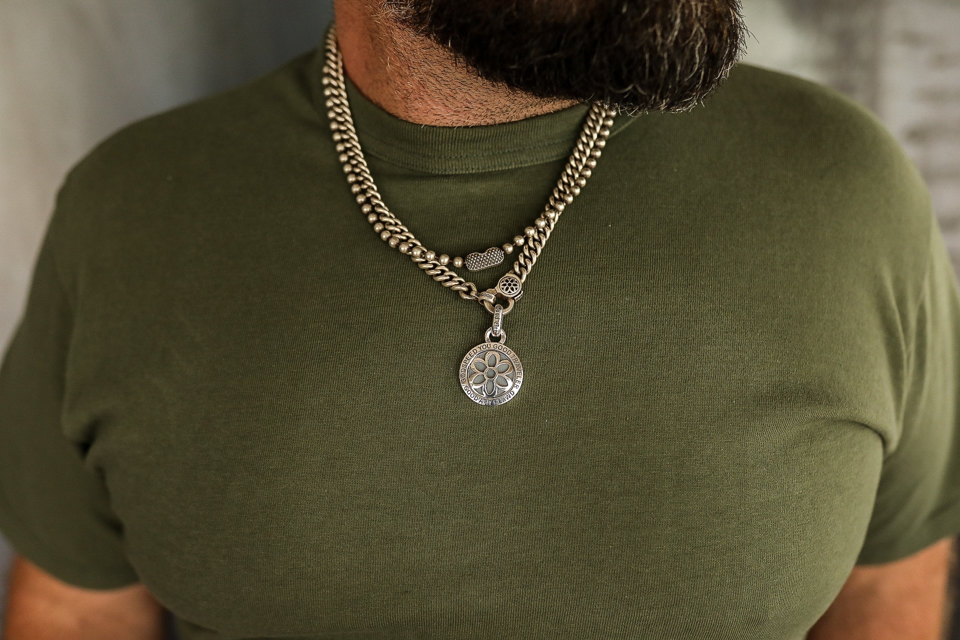 Close-up of man wearing layered silver chain necklaces with round pendant on green shirt