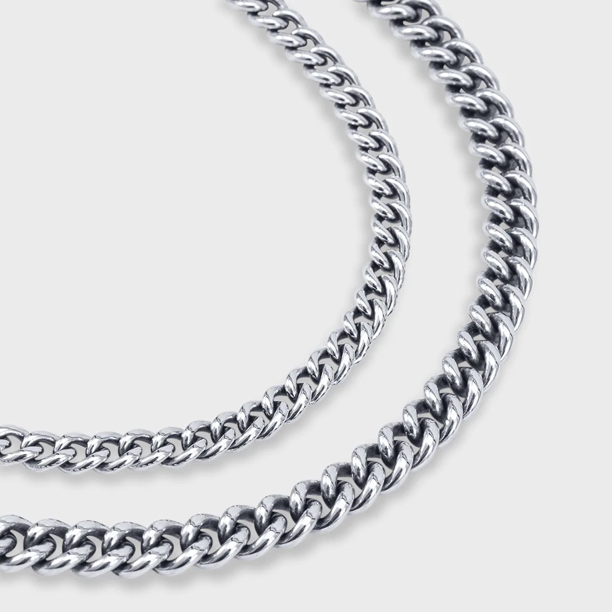 Close-up of two sterling silver curb chain necklaces with polished interlocking links on a light background