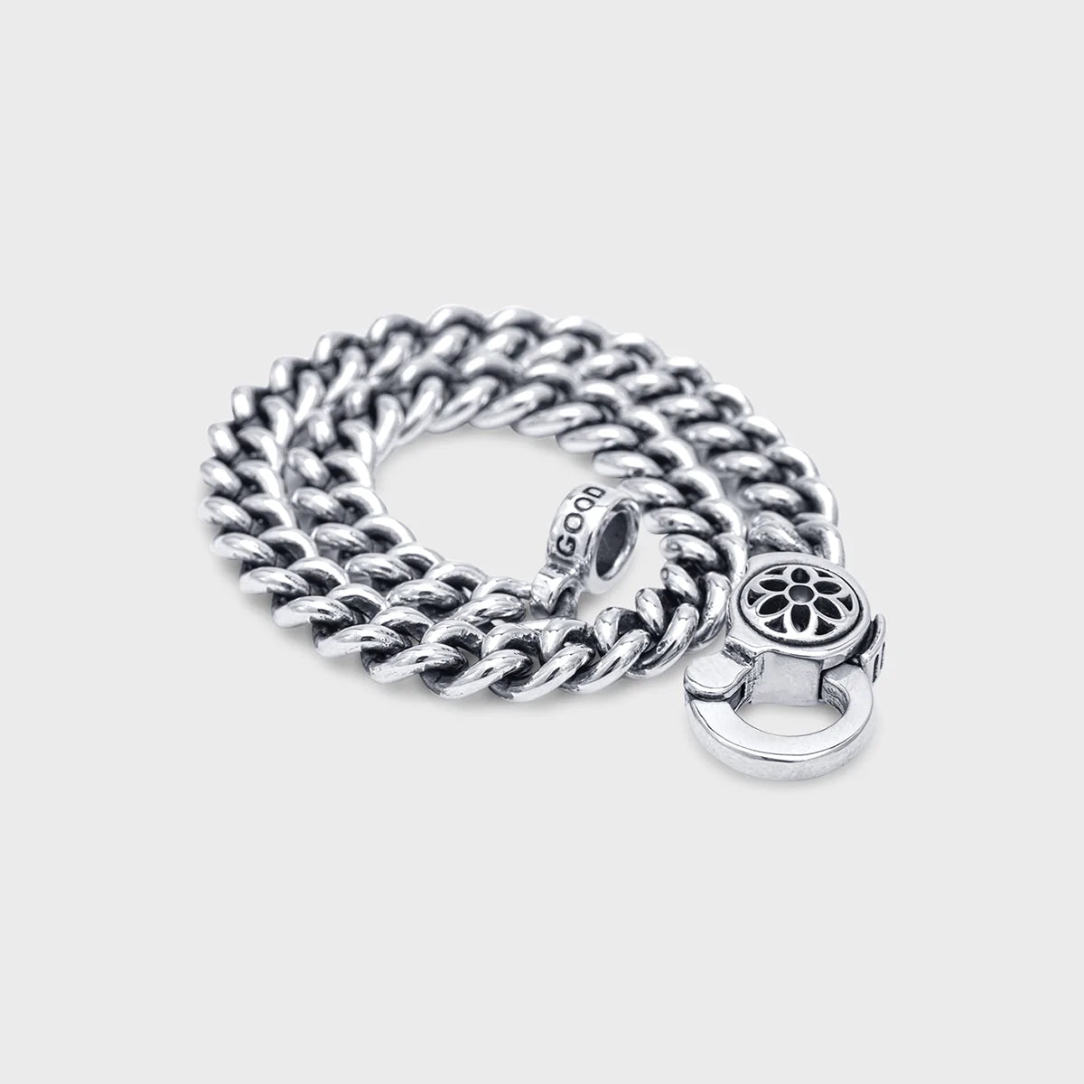 Sterling silver curb chain bracelet with flower design clasp, coiled on light background