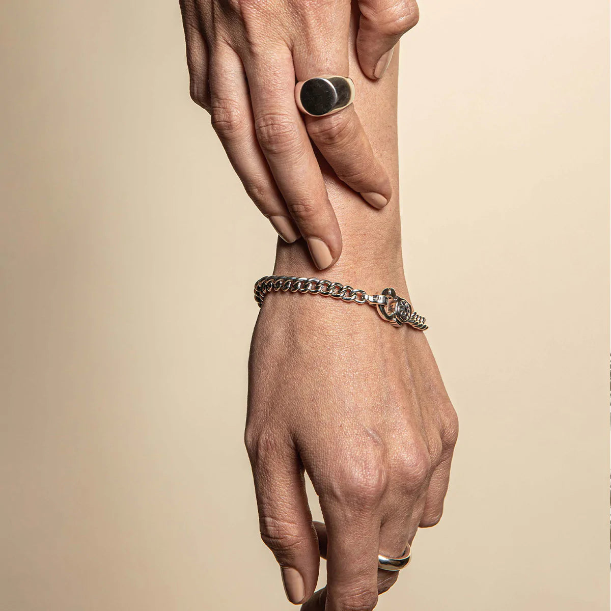 Sterling silver curb chain bracelet with toggle clasp on wrist, paired with silver rings and neutral nail polish