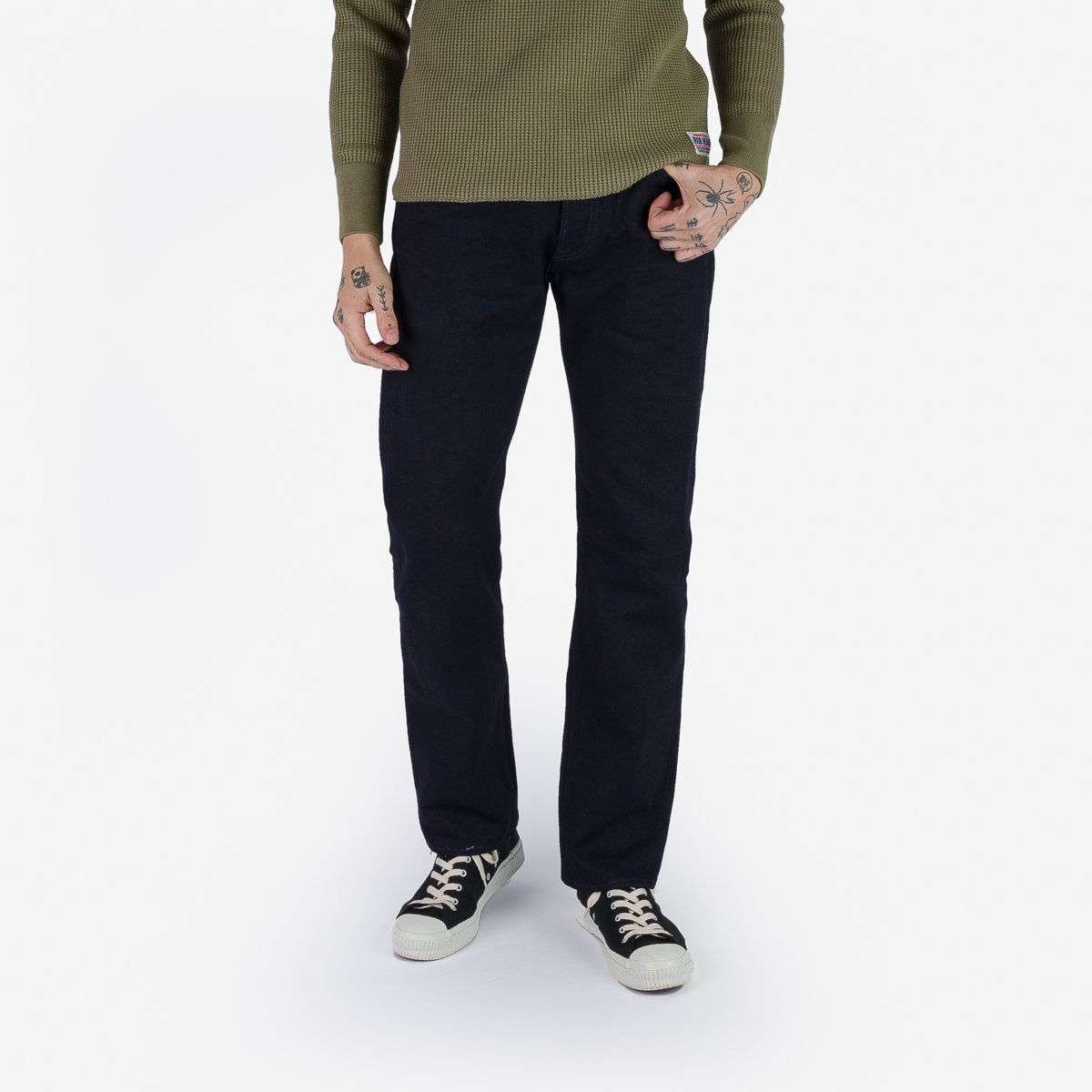 Man wearing black straight leg jeans, olive waffle knit sweater, and black canvas sneakers on white background
