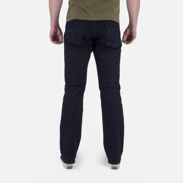 Back view of person wearing dark navy straight leg jeans and green shirt on white background
