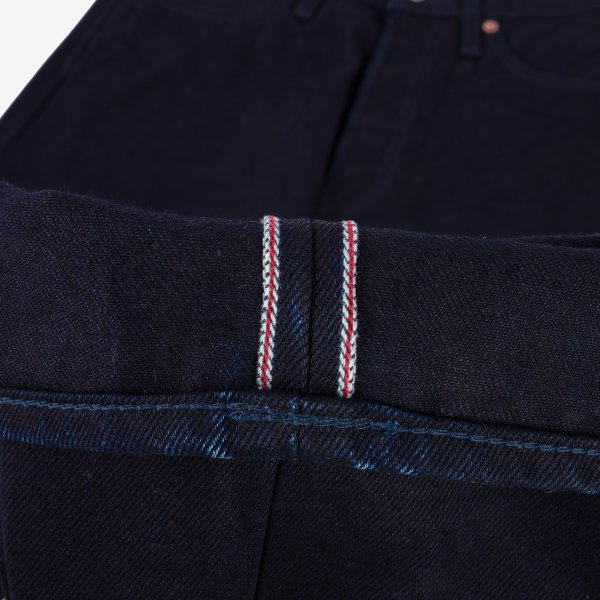 Close-up of dark raw denim jeans with selvedge edge featuring red and white stitching detail
