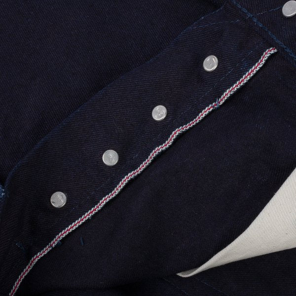 Close-up of dark raw selvedge denim with metal buttons and signature red-white-blue edge stitching