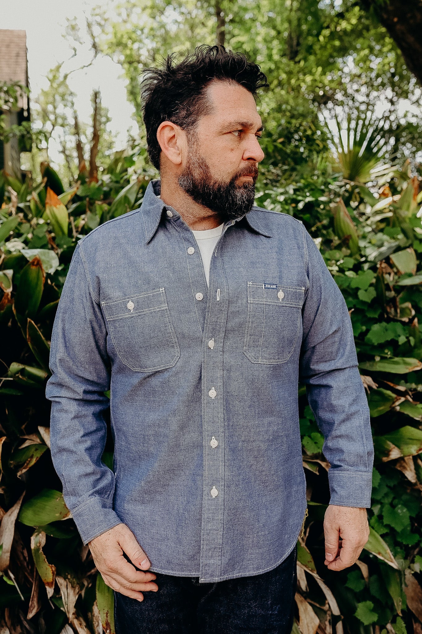 A person standing outdoors wearing a long-sleeved blue chambray work shirt with vintage-style buttons.