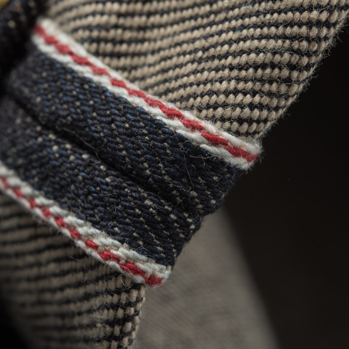 Close-up of selvedge denim fabric with beige and navy twill weave, accented by red and white stitching